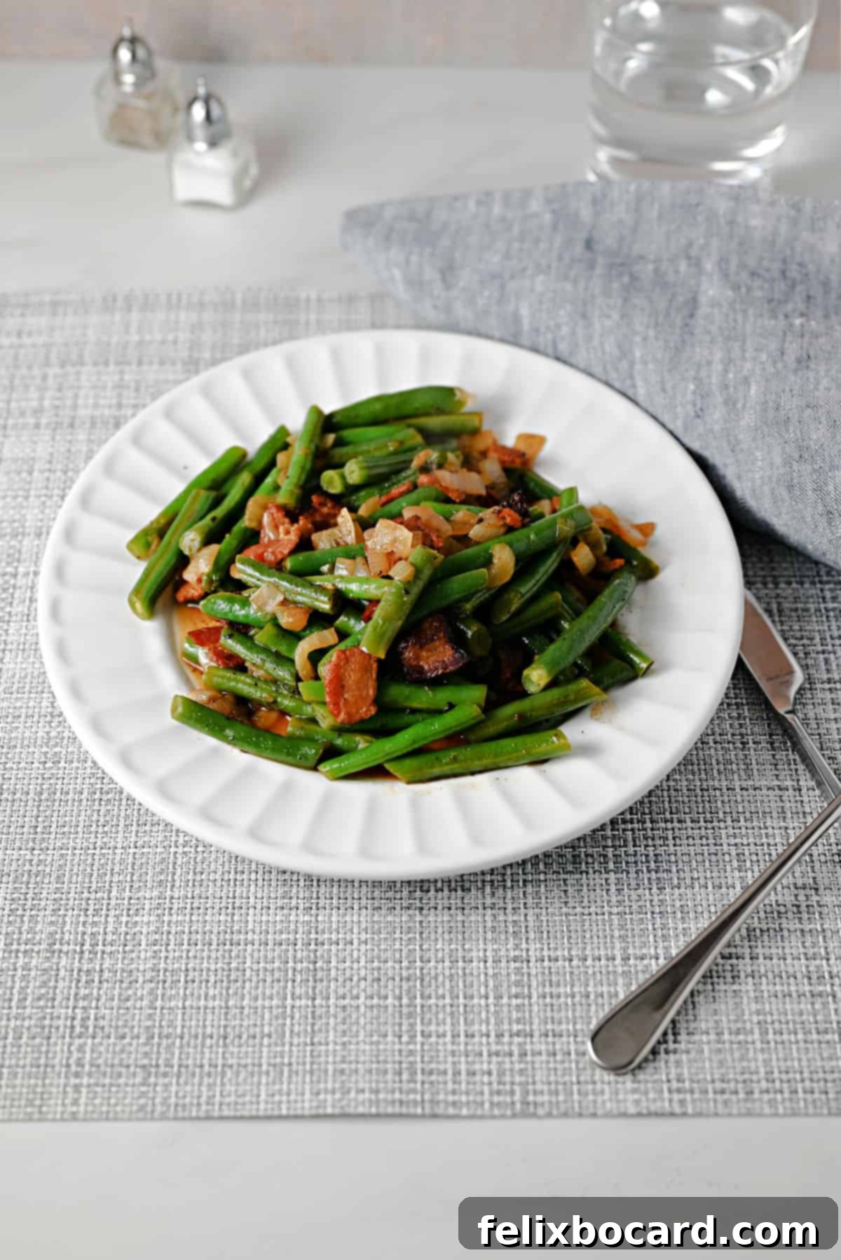 Plate of Texas Roadhouse style green beans with visible bacon and savory sauce, ready to be enjoyed.