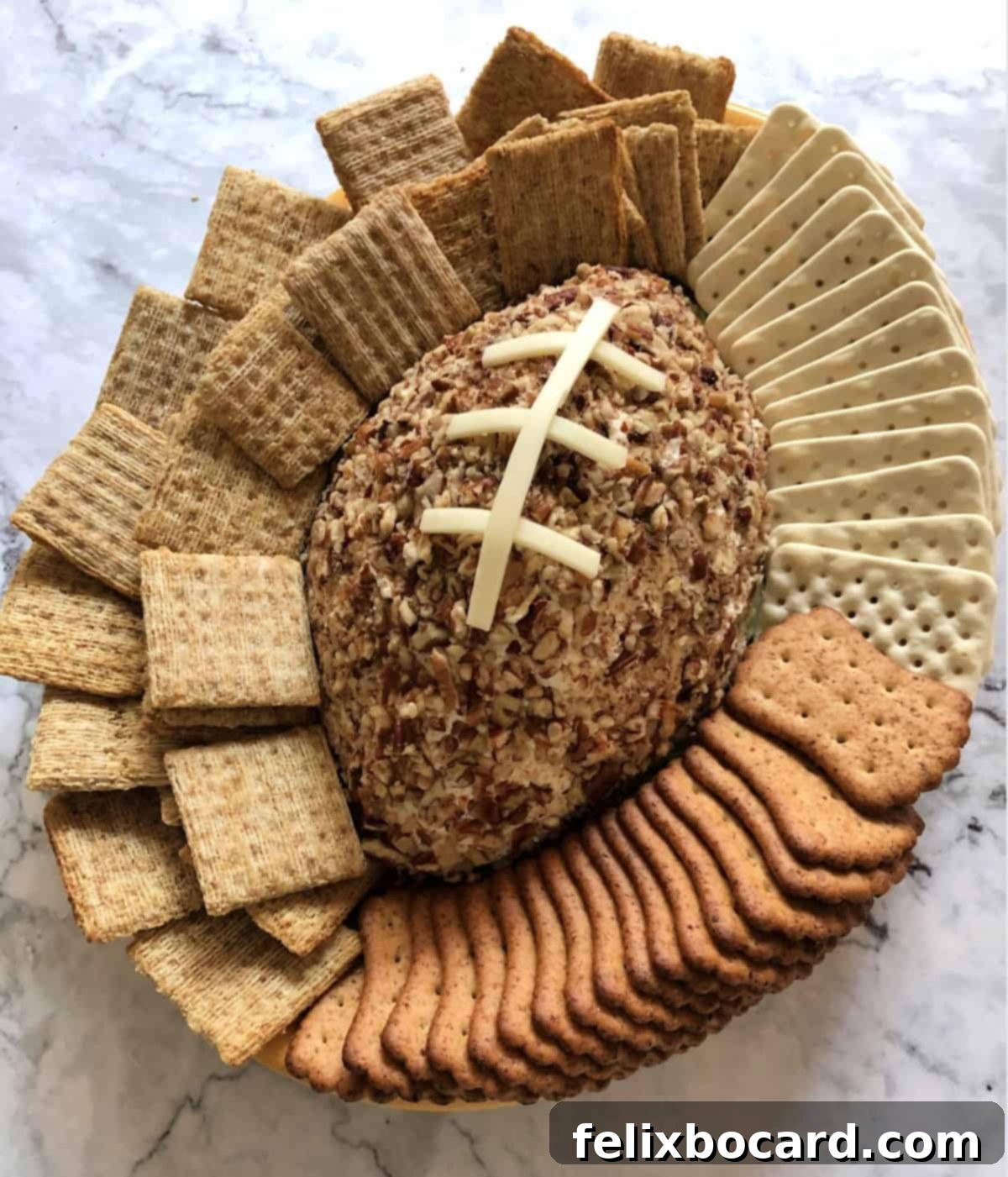 Football shaped Cheeseball on a serving platter surrounded by crackers, a perfect game day snack.