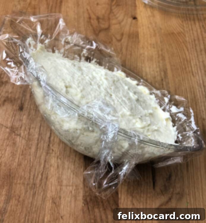 Cheese ball mixture spooned into a plastic football-shaped mold lined with plastic wrap.