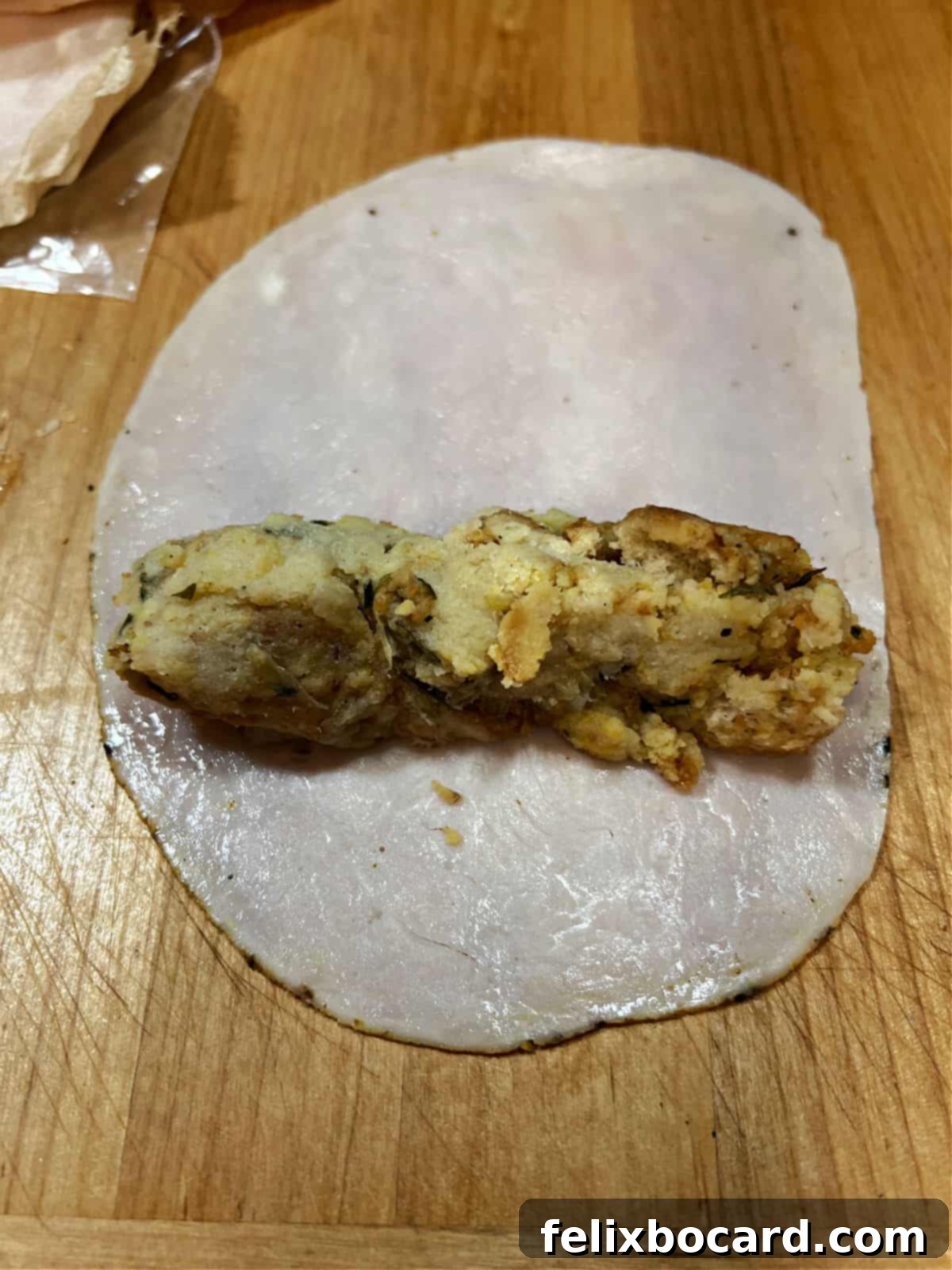 A scoop of prepared stuffing is carefully placed onto a slice of deli turkey, ready to be formed into a log and rolled.