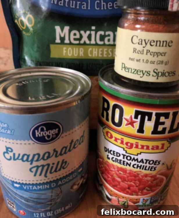 Key ingredients for homemade queso dip: a bag of Mexican blend cheese, a jar of vibrant red cayenne pepper, a can of evaporated milk, and a can of Rotel tomatoes with green chilies, neatly arranged.