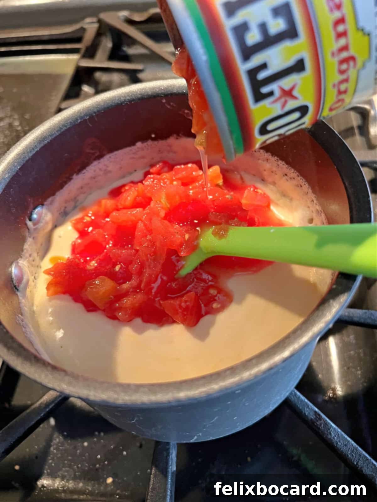 A can of diced Rotel tomatoes with green chilies being poured into a saucepan of melted cheese and evaporated milk, ready to be stirred.
