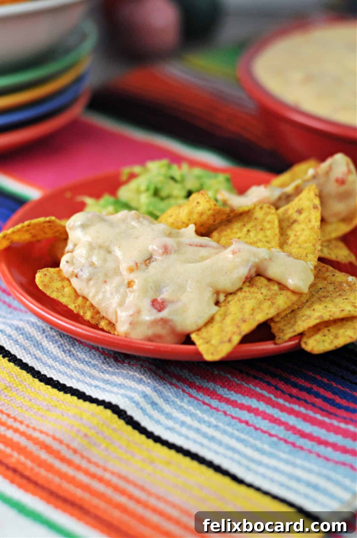 An enticing plate of loaded nachos featuring crispy tortilla chips generously topped with creamy homemade queso dip and a dollop of fresh guacamole on the side, ready for a delicious snack.