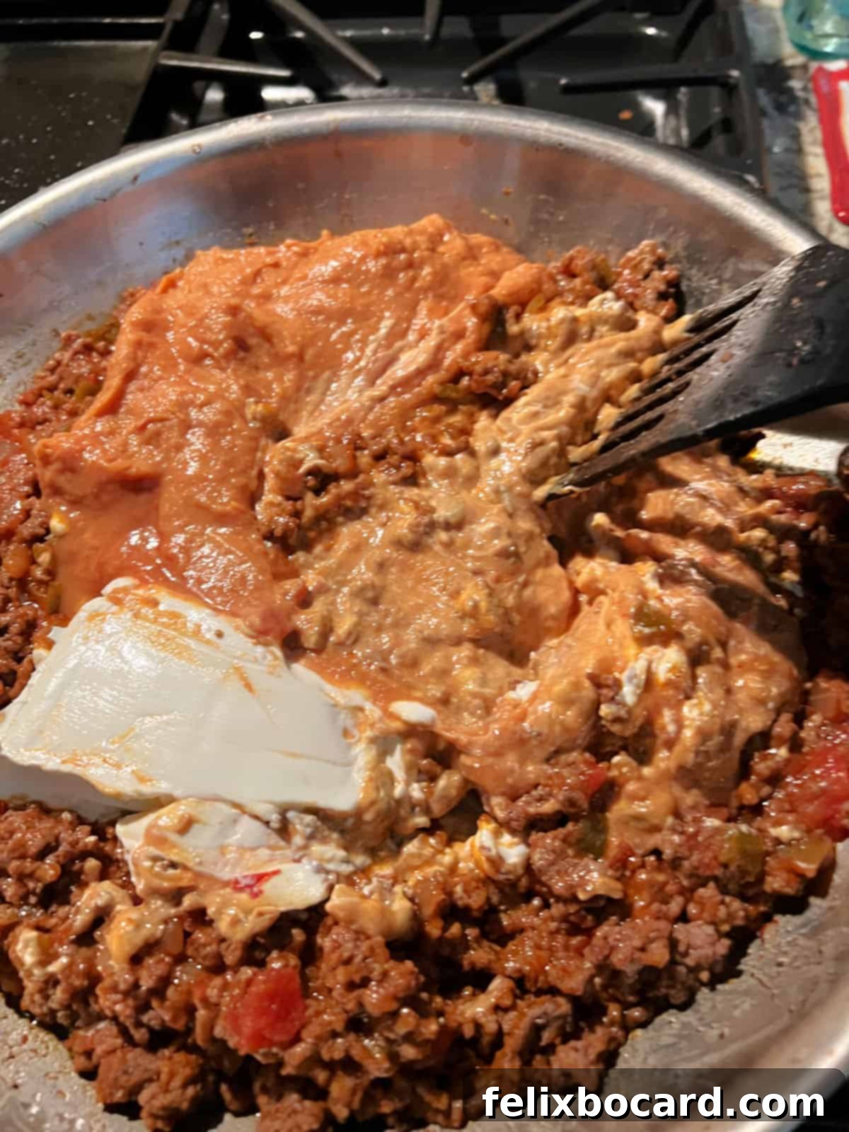 Stirring to incorporate the cream cheese and beans into the beef mixture in a skillet.