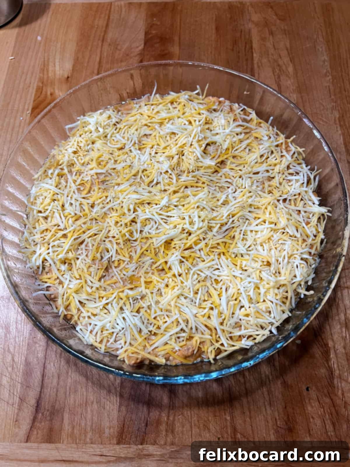 Hot taco dip mixture in a baking dish, topped generously with shredded cheese, ready for the oven.