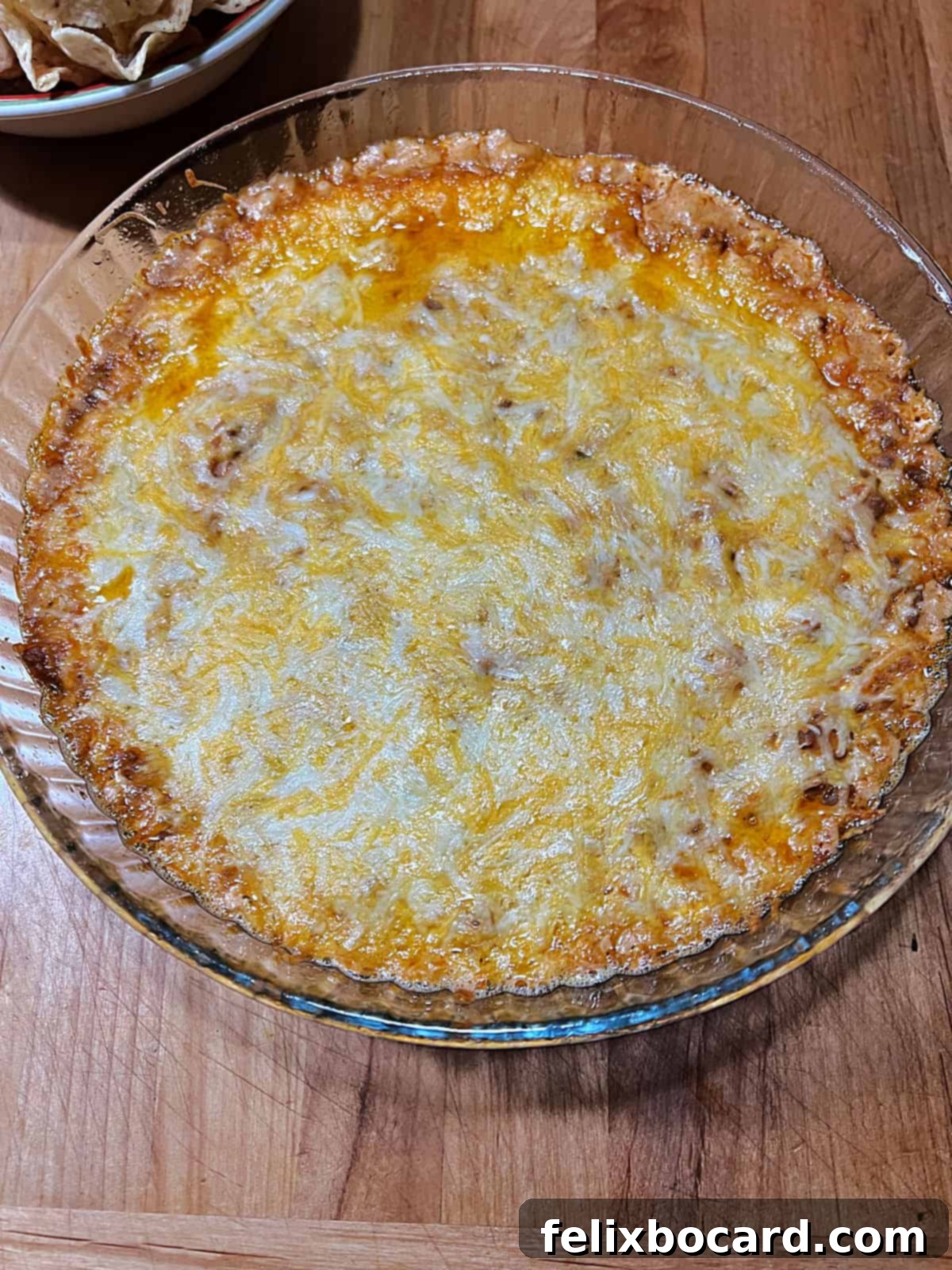 Hot baked taco dip with bubbly edges and perfectly melted, golden cheese, fresh out of the oven.