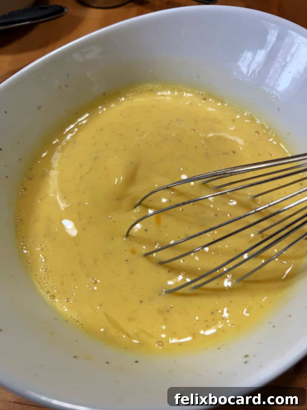 Savory Sausage and Egg Cups 6 Close-up of a whisk mixing eggs with milk or cream in a glass bowl.