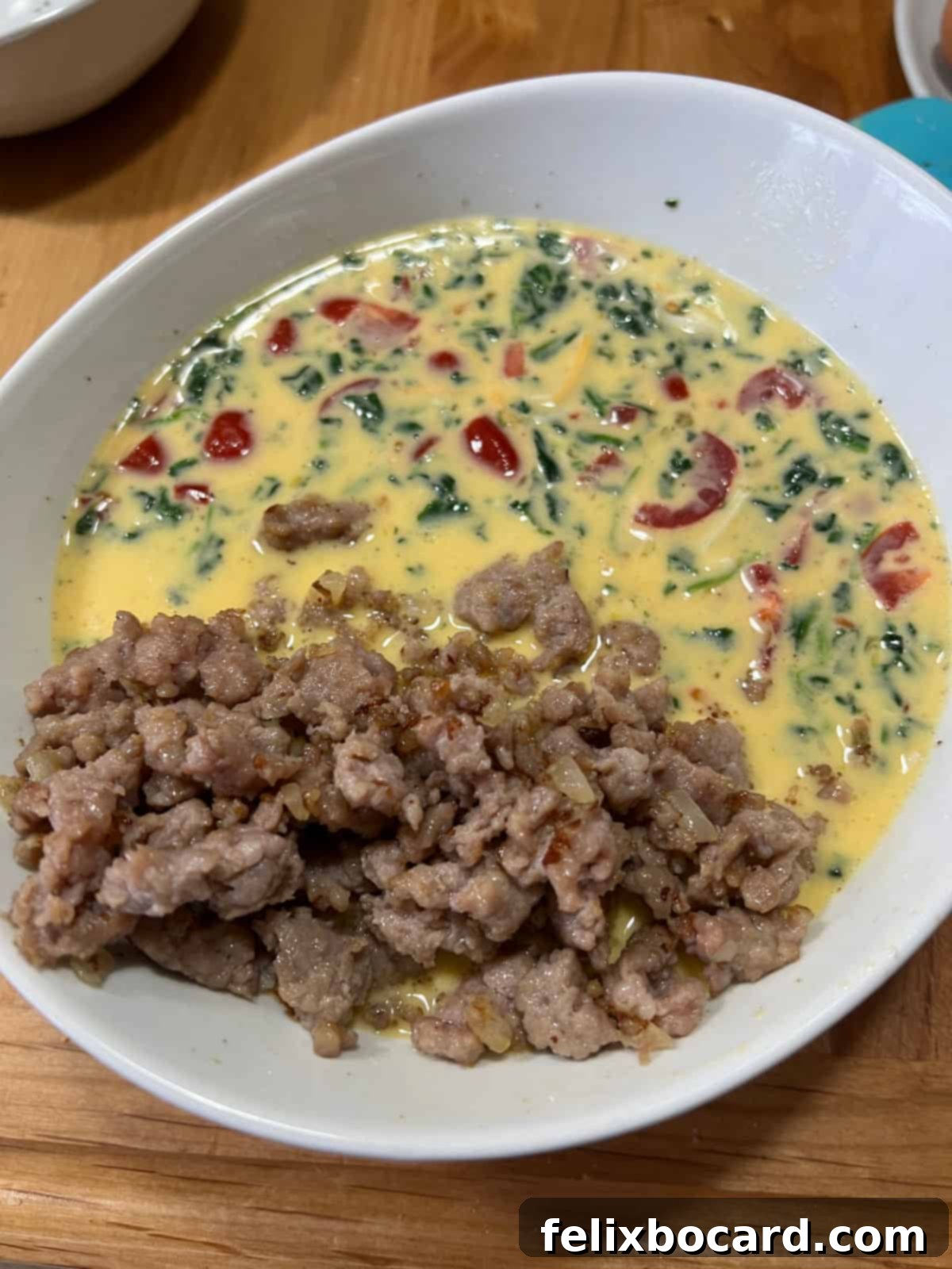 Savory Sausage and Egg Cups 7 Adding cooked sausage crumbles to a bowl of whisked eggs, spinach, tomatoes, and shredded cheese.