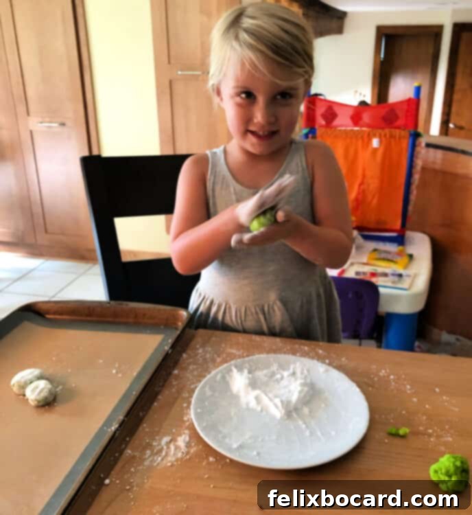 Spooky Eyeball Treats 4 A smiling child's hands carefully rolling cookie dough into a ball, coated in powdered sugar.