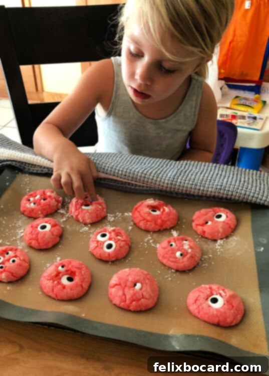 Spooky Eyeball Treats 5 A child's hands carefully placing edible candy googly eyes onto warm, freshly baked monster cookies.