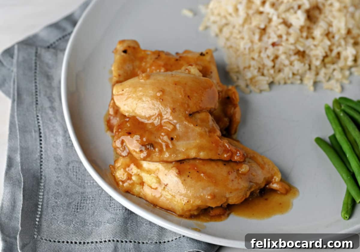 Top down view of chicken thighs with apricot sauce on a plate with rice and green beans.