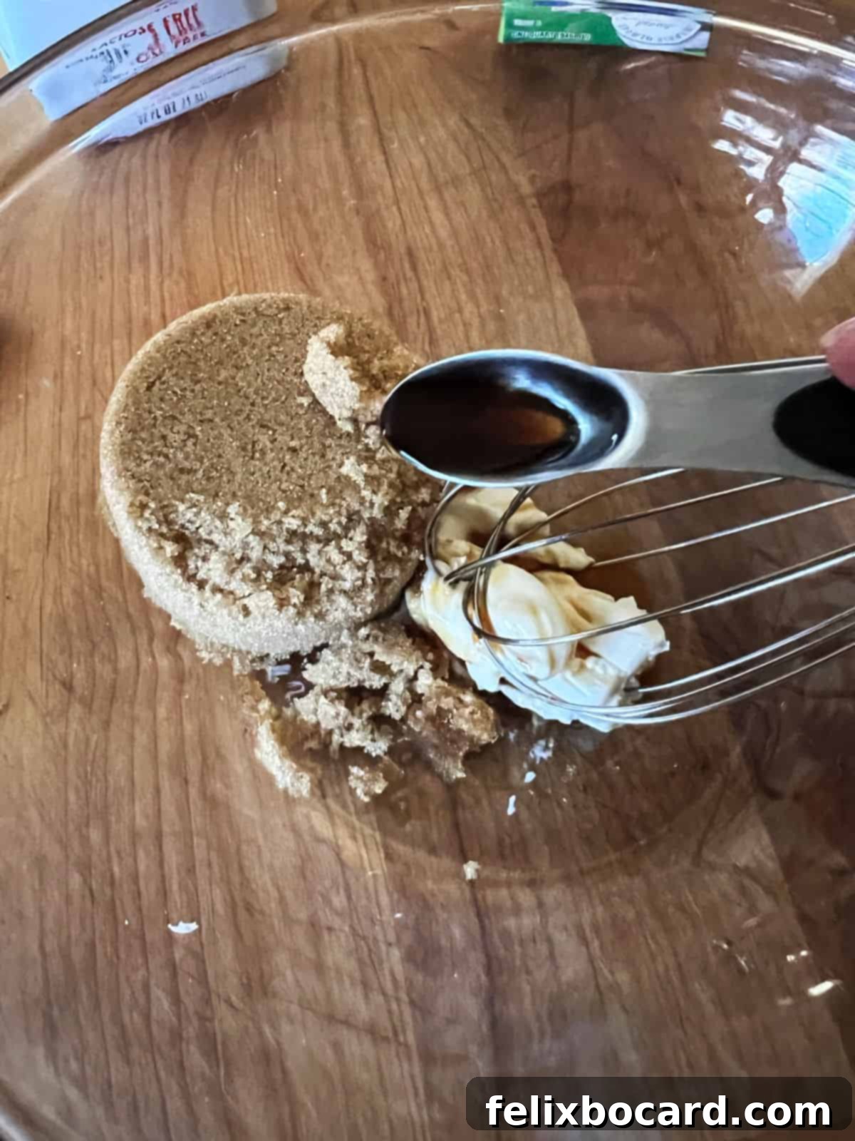Cream cheese, brown sugar, and vanilla extract are whisked together in a bowl, forming a smooth, thick paste, the first step in preparing the ice cream base.