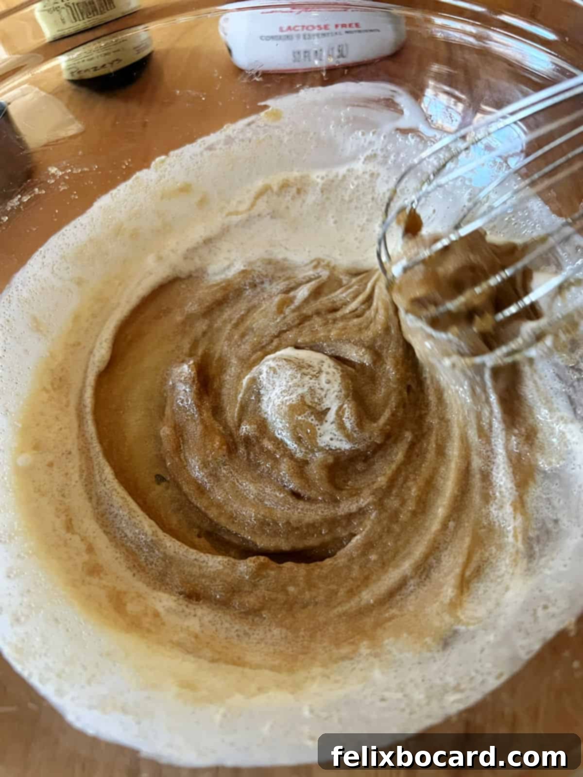 A whisk incorporates the first small amount of heavy cream into the brown sugar and cream cheese mixture, ensuring a smooth, lump-free base.