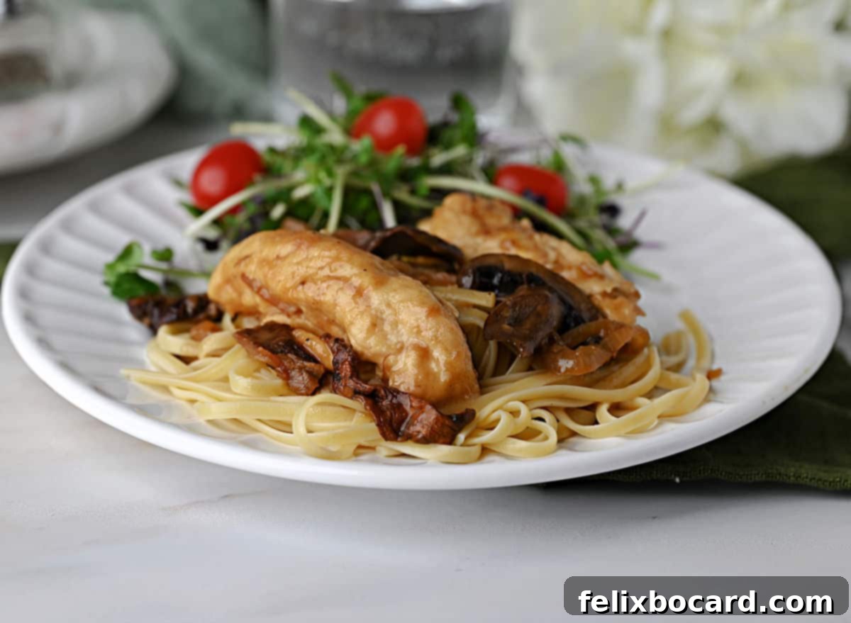 A beautifully plated dish of Chicken Marsala with fettuccine noodles and a vibrant green salad.