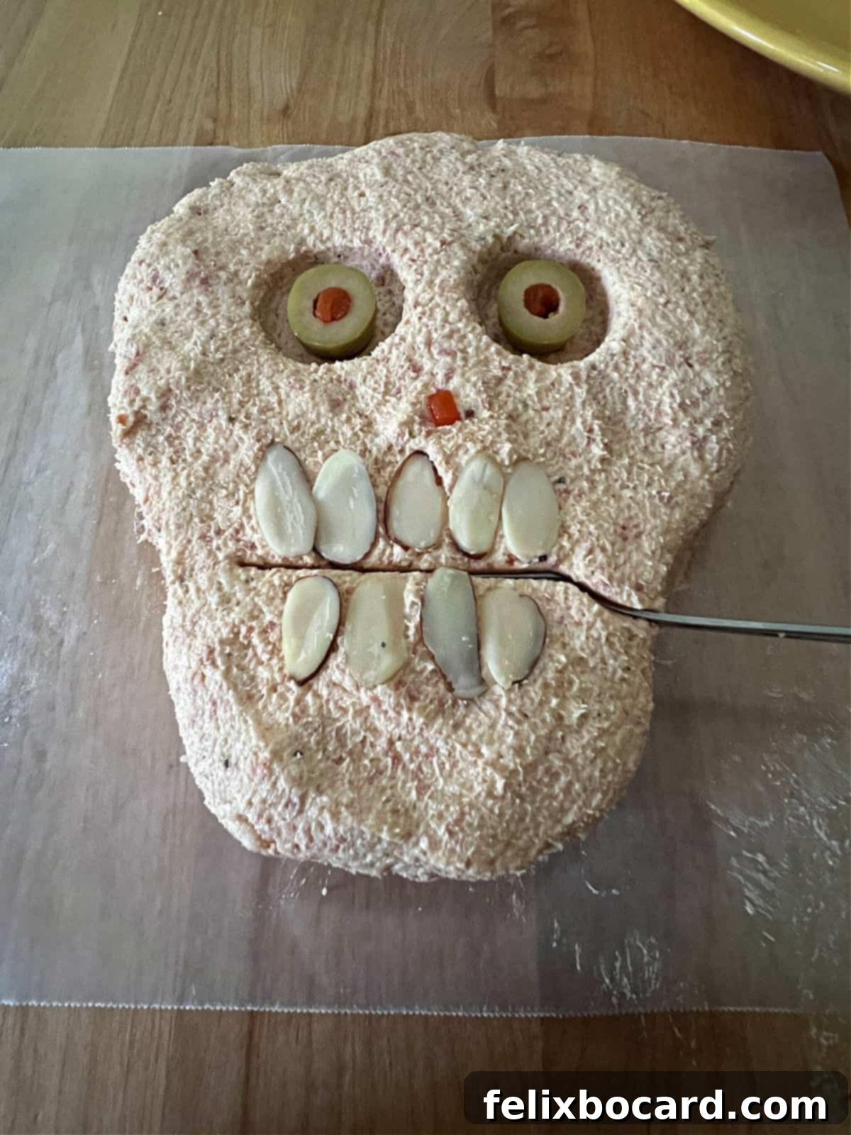 Spooky Pepperoni Skull Cheeseball 9 serving knife inserted between the almonds.