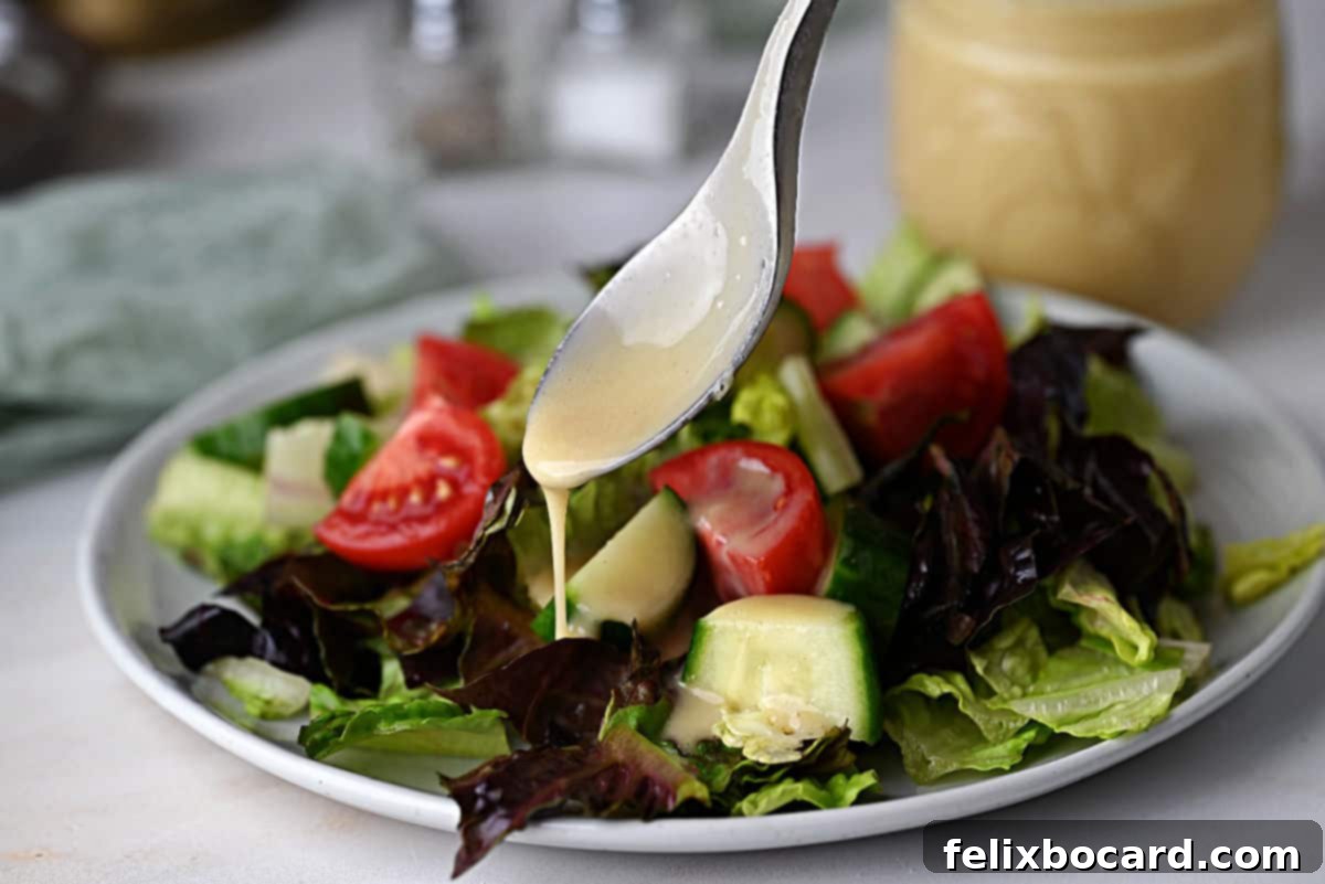 A spoon full of homemade honey lime dressing getting drizzled onto a fresh green salad, highlighting its perfect consistency and vibrant color.