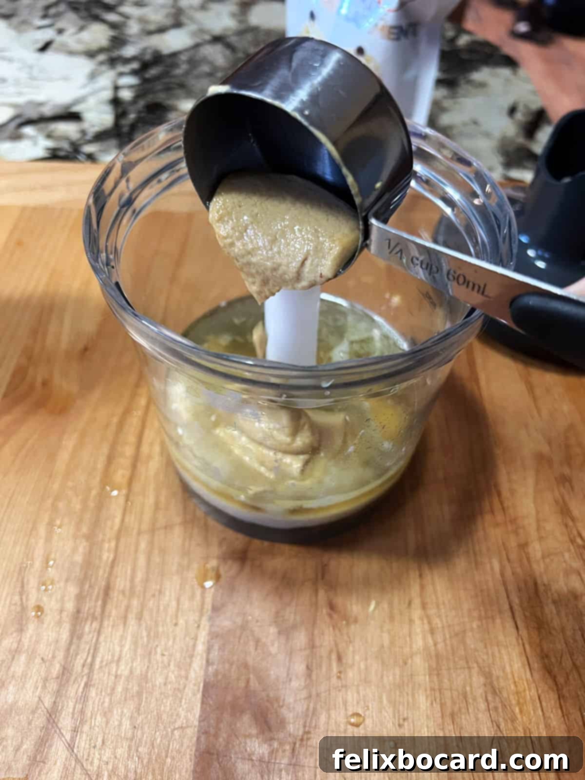 Adding a spoonful of Dijon mustard into a blender container, showing the first step of preparing the dressing.