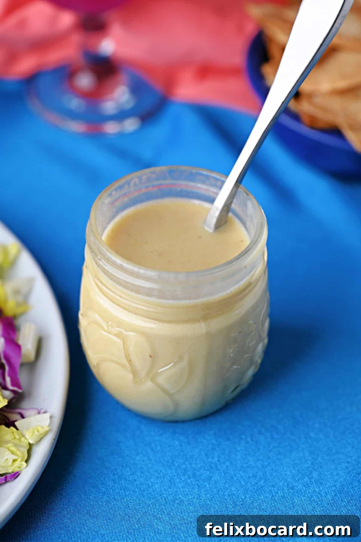 A small glass jar filled with golden honey lime dressing, with a spoon resting beside it, ready for use on a salad.