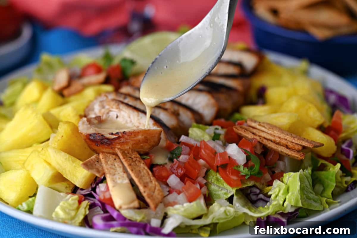 A spoon drizzling dressing over the chicken on the caribbean salad.