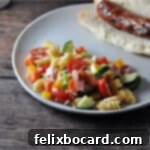 A serving of easy pasta salad, vibrant and flavorful, presented on a plate alongside a grilled brat in a bun for a complete meal.