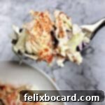 A fork lifts a generous helping of creamy coleslaw from a rustic wooden bowl, with the full bowl blurred in the background, highlighting the fresh ingredients.