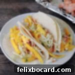 Three soft-shell fish tacos, generously topped with vibrant mango slaw, arranged enticingly on a serving dish.