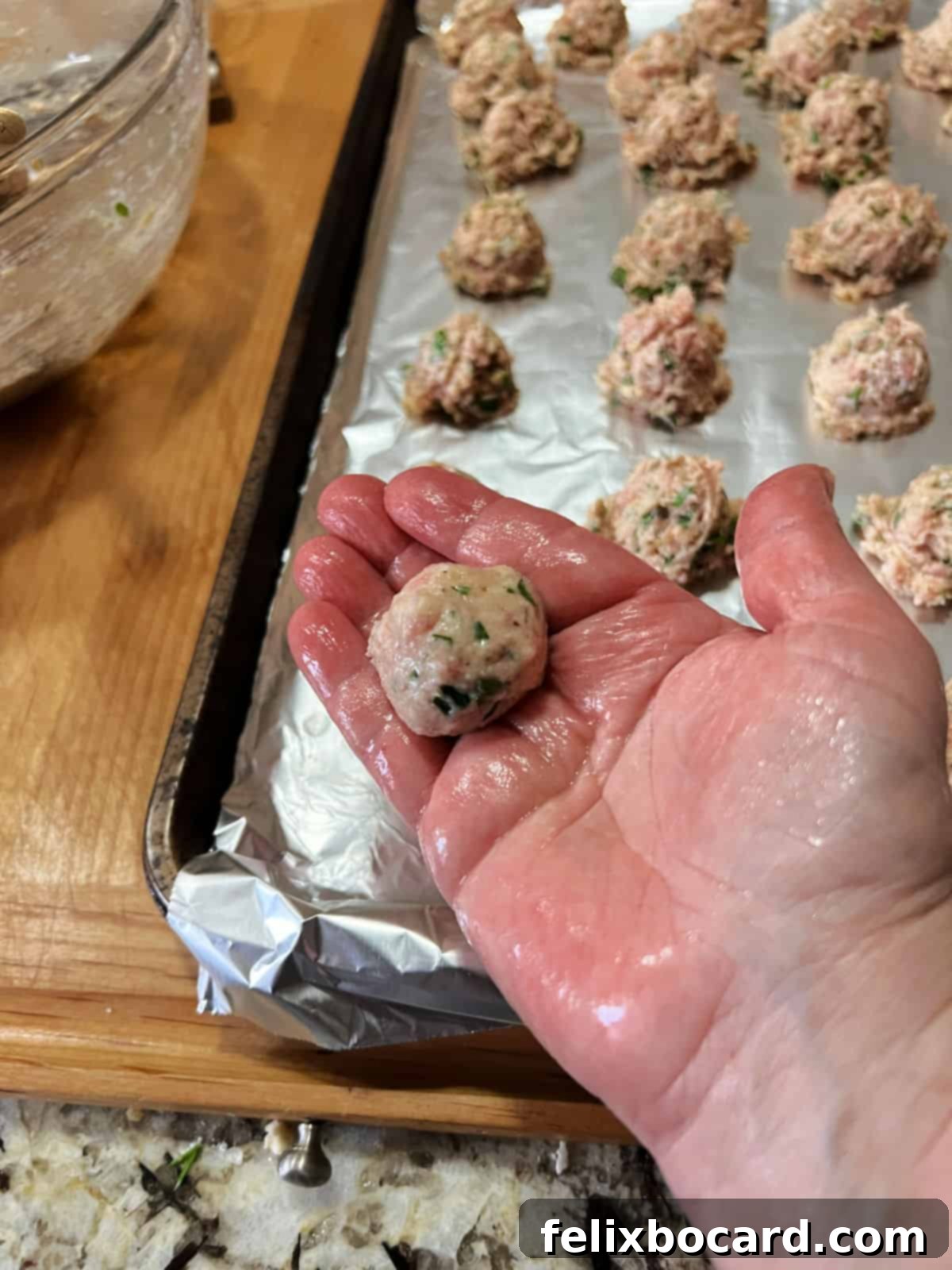 A wet hand gently rolling a portion of the meatball mixture into a perfect ball shape.