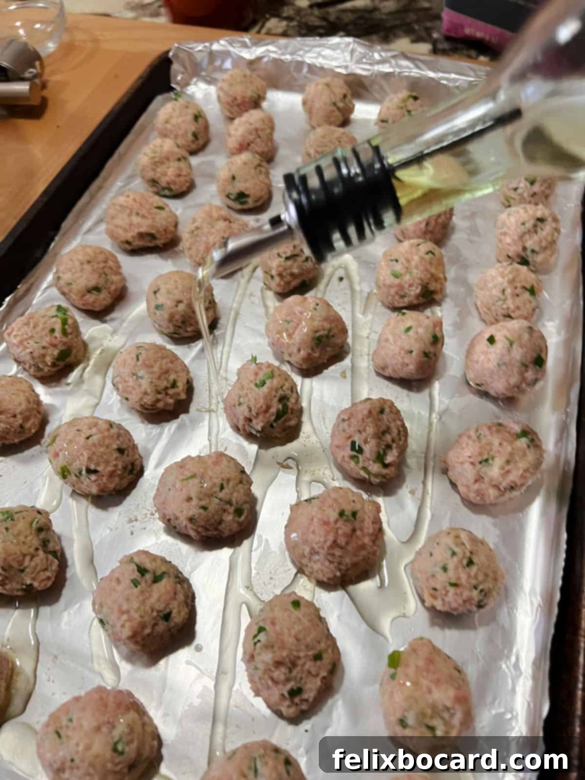 Drizzling olive oil over the neatly arranged chicken ricotta meatballs on a parchment-lined baking sheet.