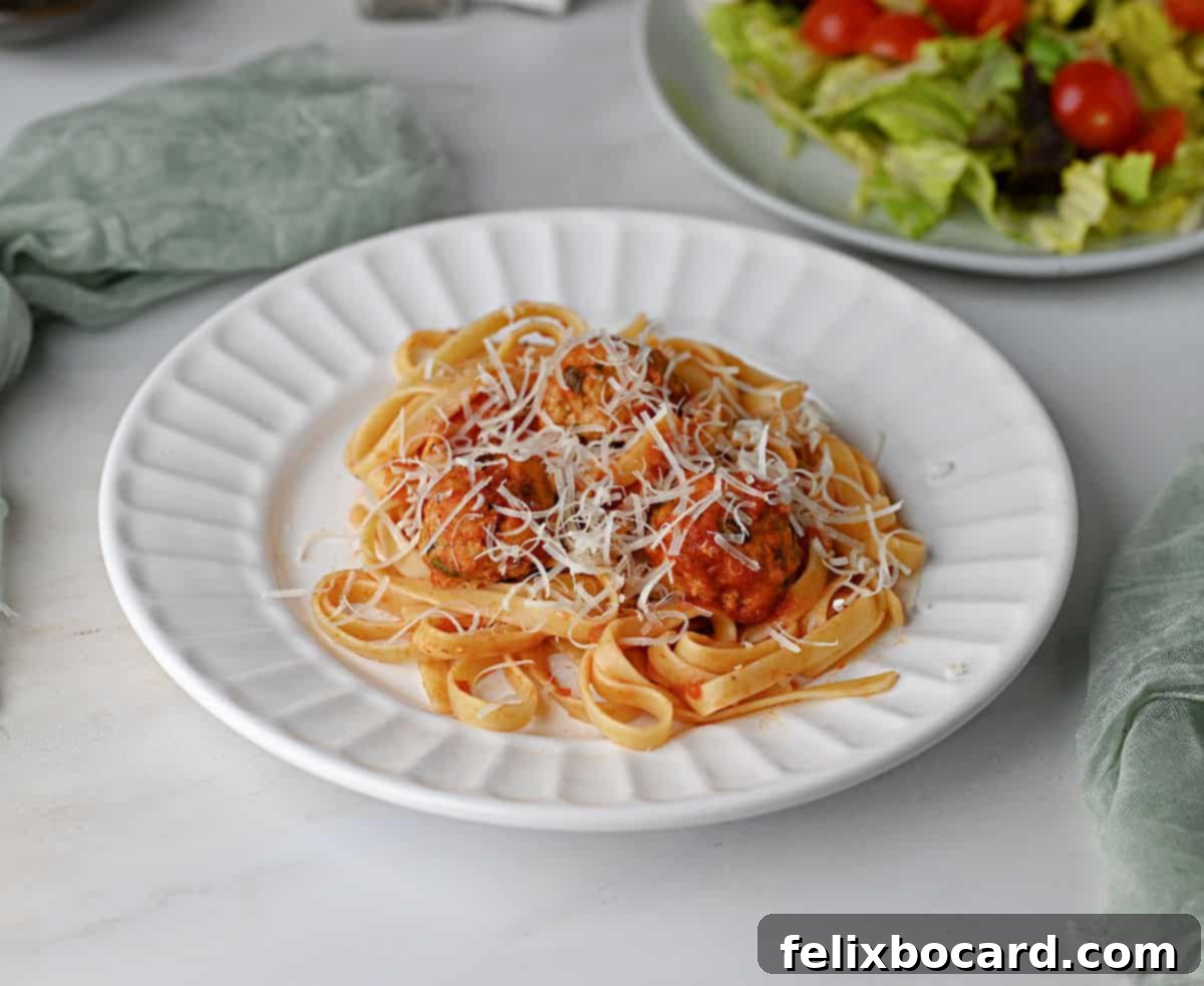 Chicken ricotta meatballs on a bed of marinara-coated pasta, generously sprinkled with shredded Parmesan cheese.
