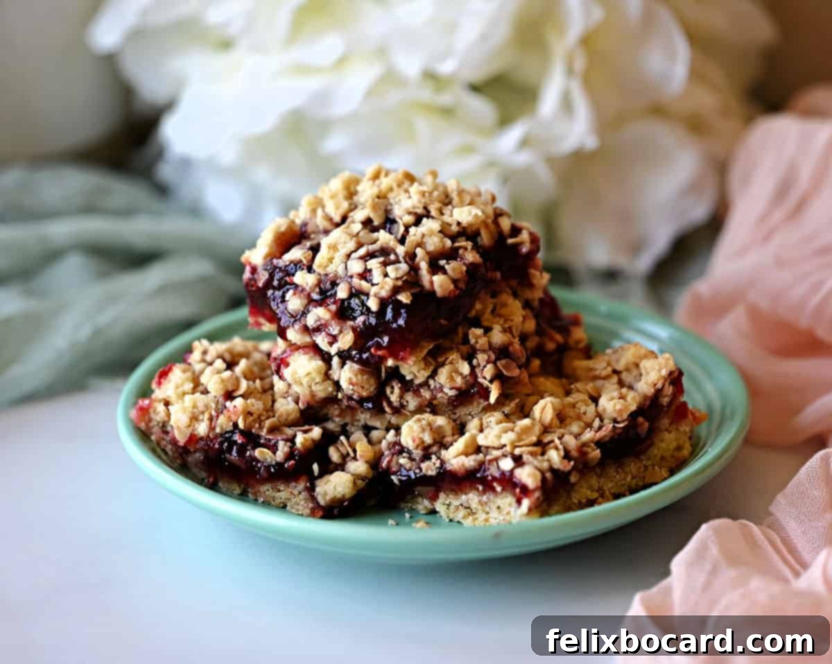 A stack of golden brown raspberry oat bars with vibrant red jam peeking through, ready to be enjoyed.