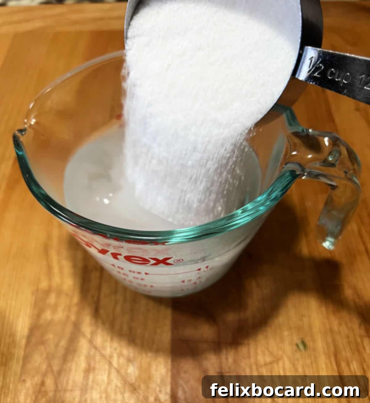 Adding sugar to warm water in a glass measuring cup.