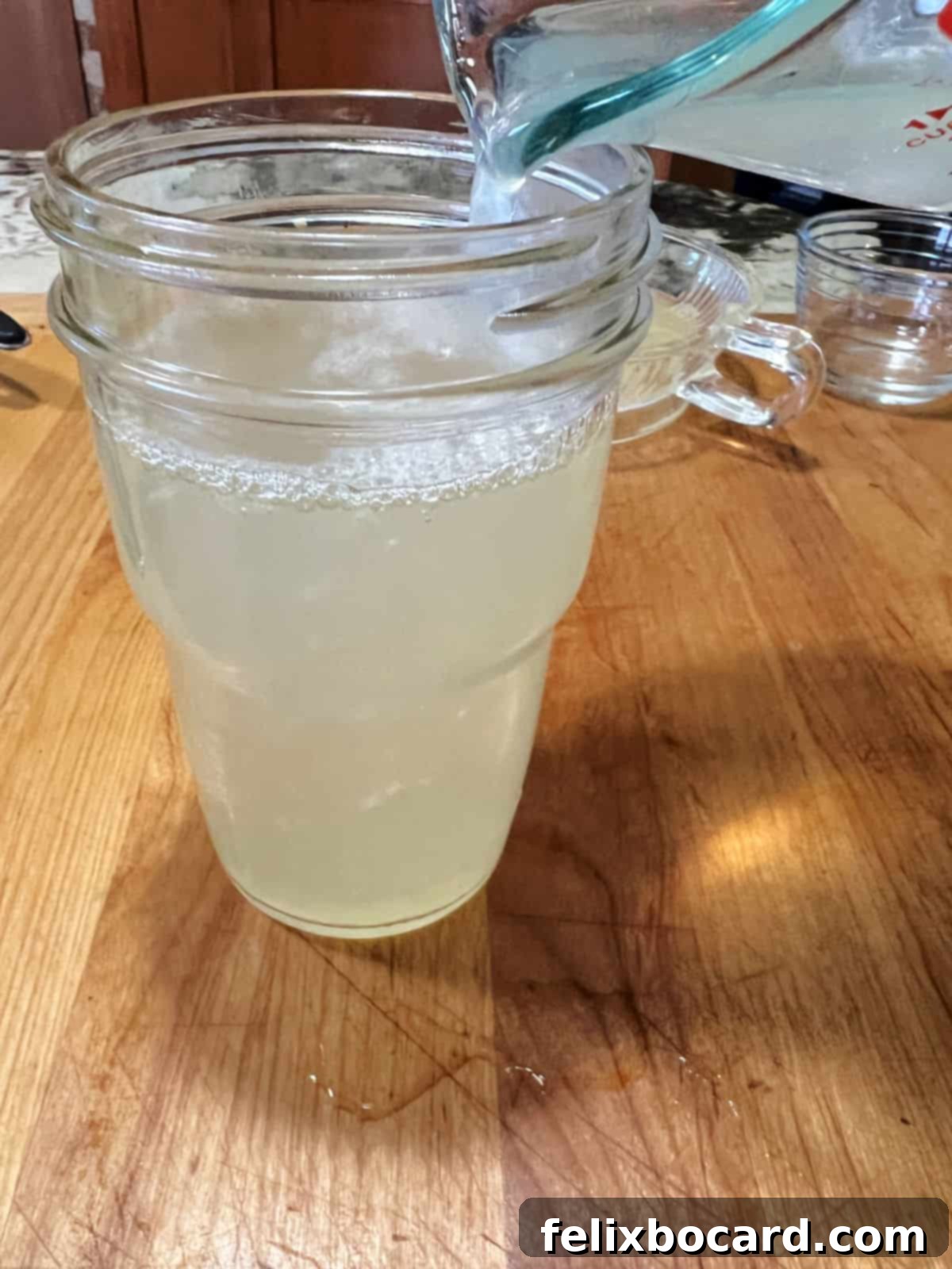Pouring homemade sweet and sour mix into a glass jar for storage.