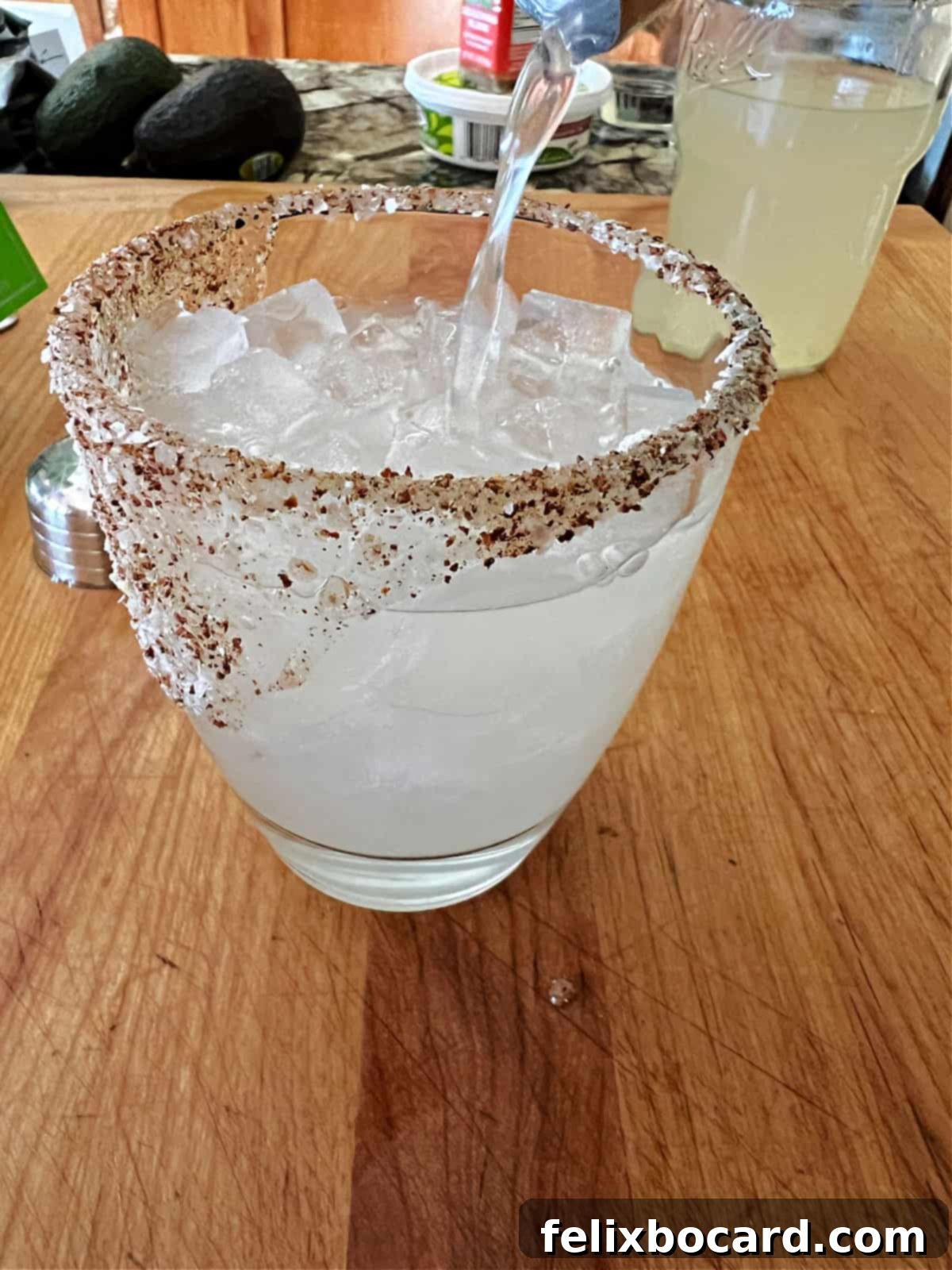The perfectly mixed margarita being poured from a shaker into a glass over ice, ready for serving.