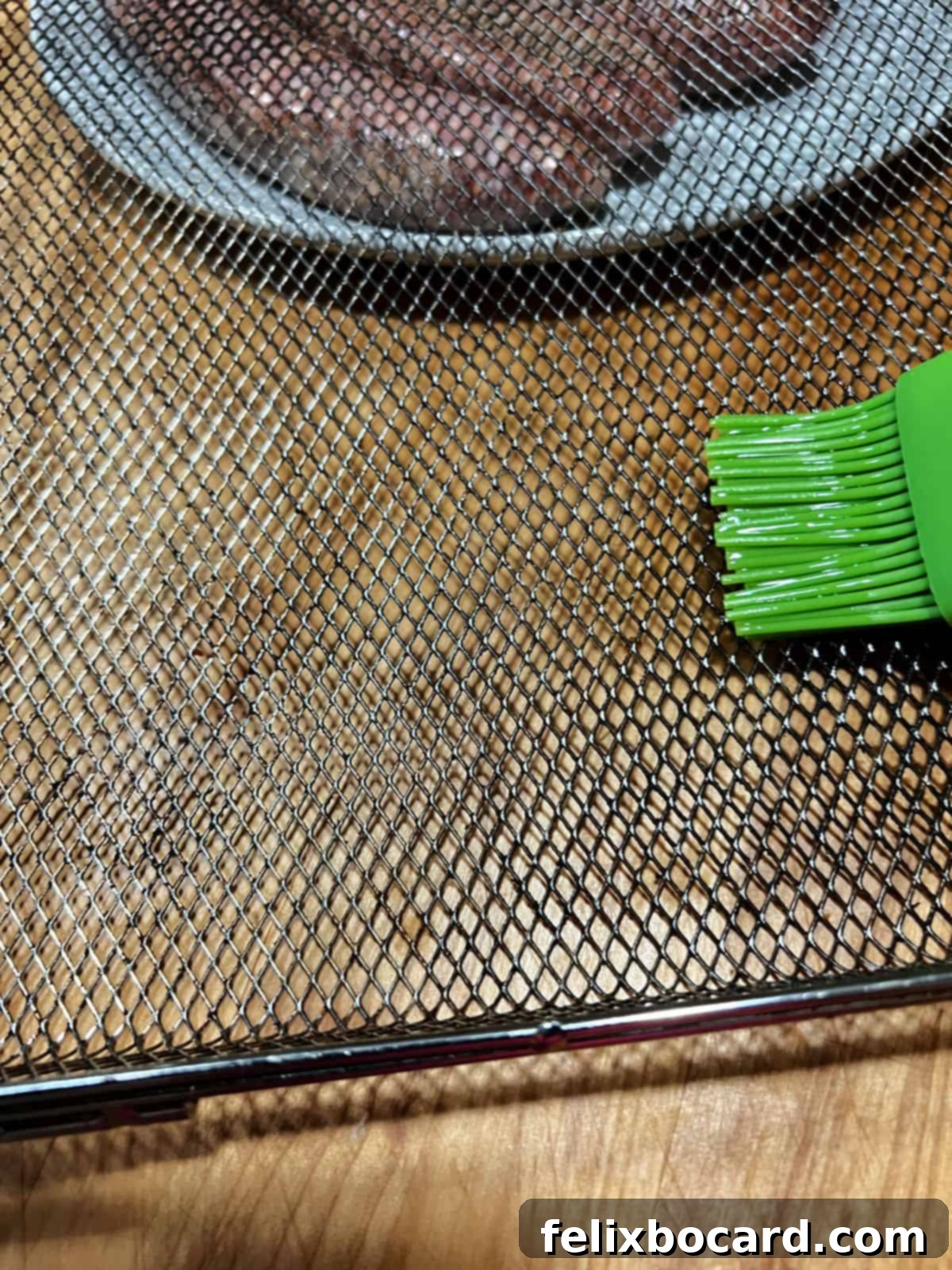 A hand brushing a small amount of oil onto the mesh surface of an air fryer basket.