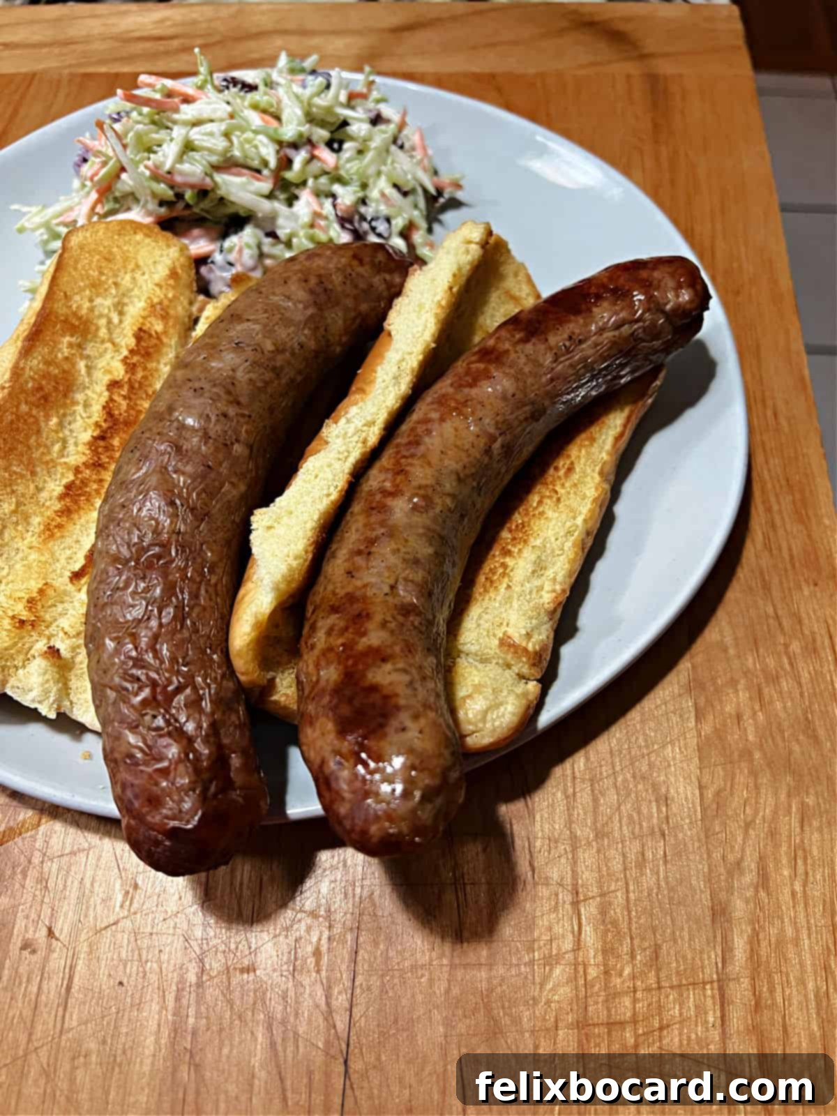 Two Italian sausages served in toasted buns with a side of coleslaw on a white plate.
