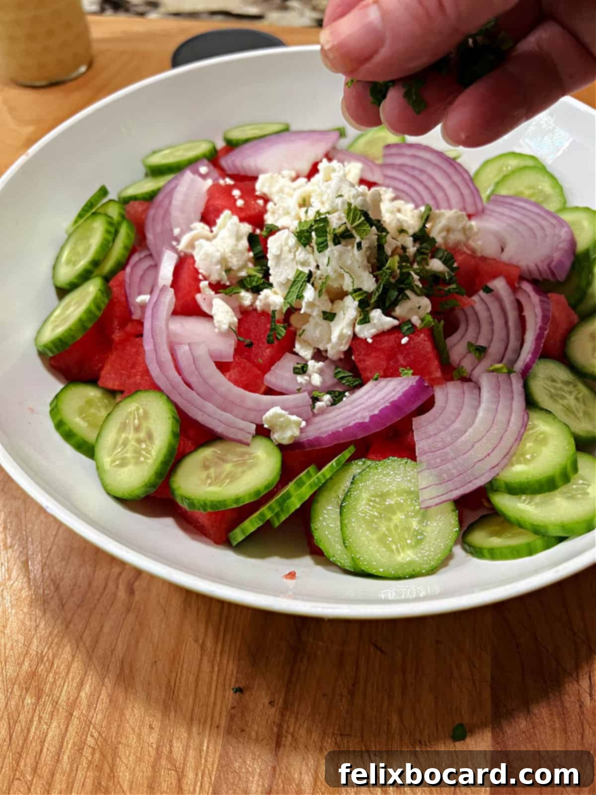 Adding chopped fresh mint to a bowl of watermelon, feta, cucumber, and red onion salad.