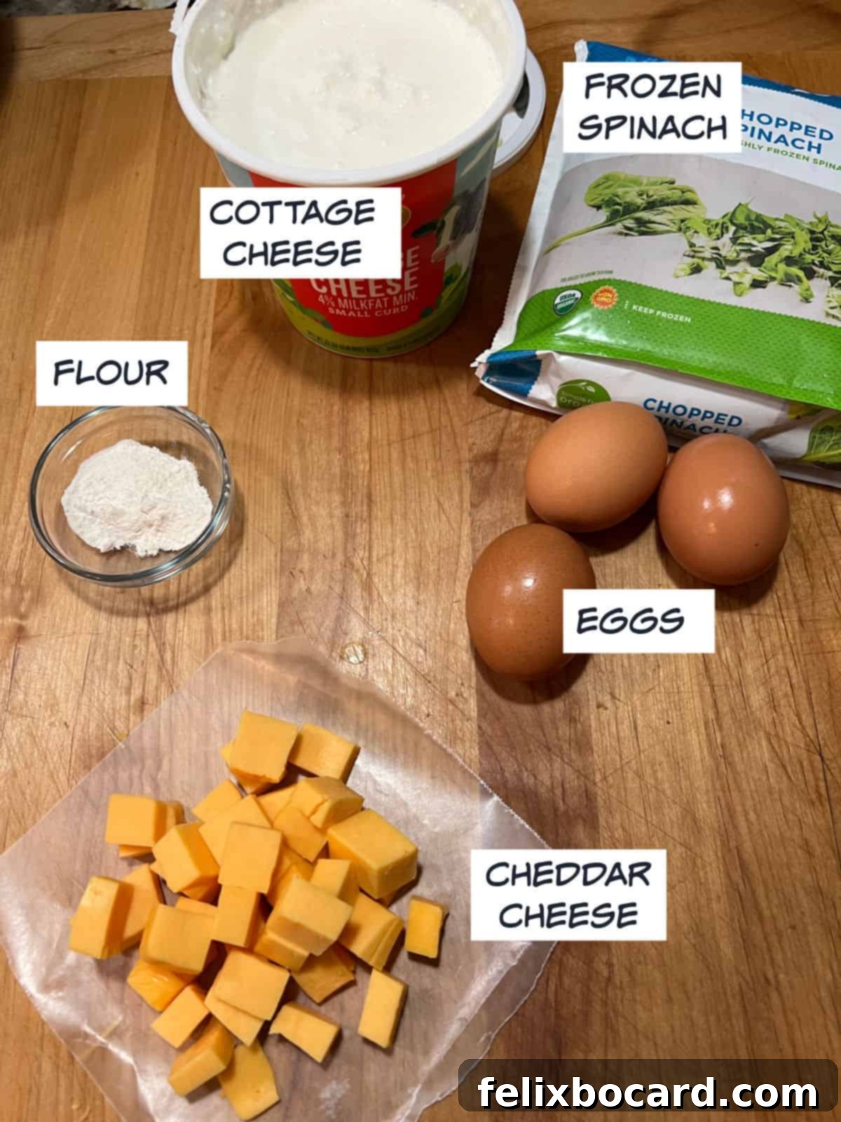 Key ingredients laid out: cottage cheese, frozen chopped spinach, fresh eggs, cubed Cheddar cheese, and flour.