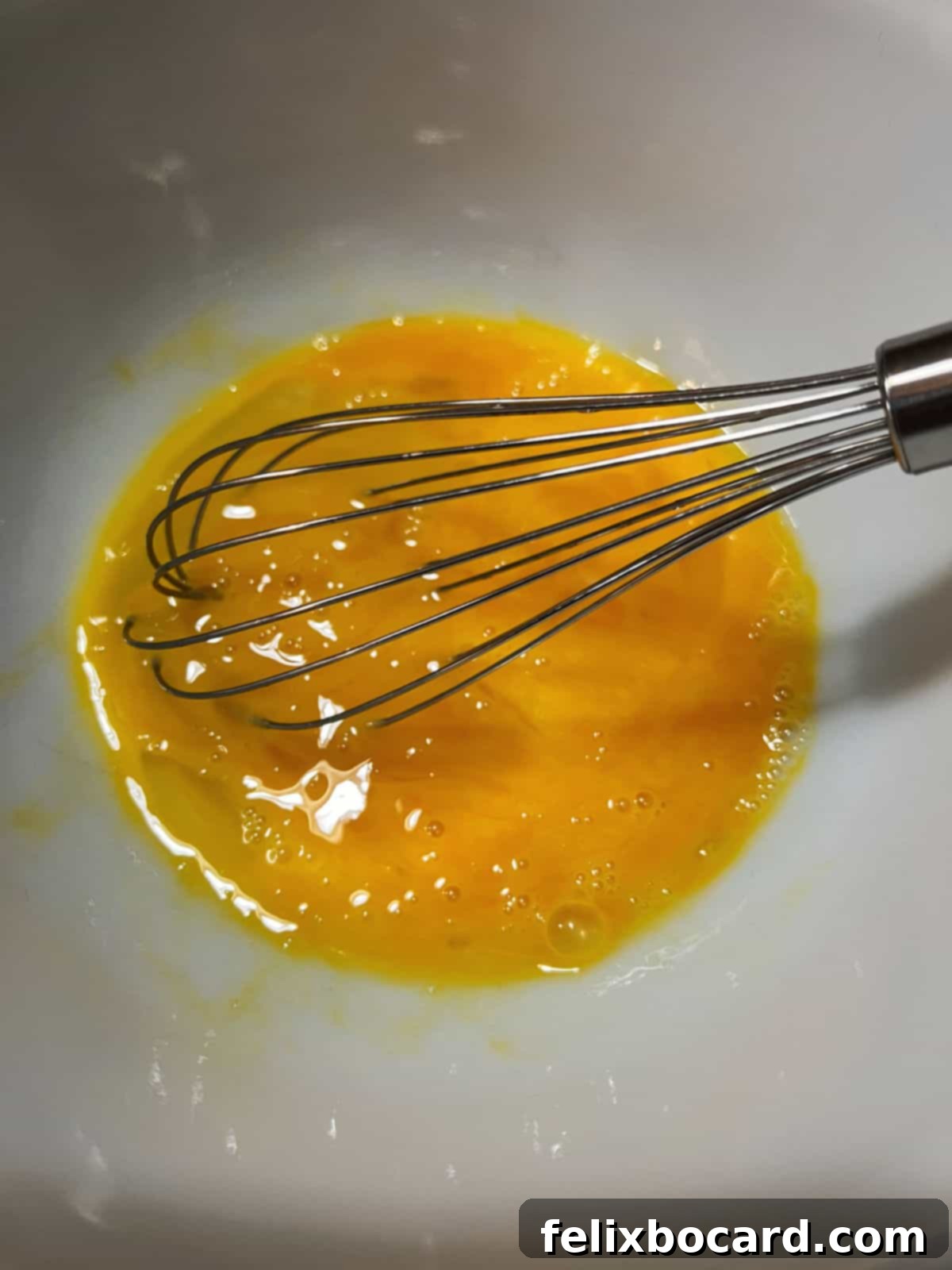 A whisk vigorously beating eggs in a spacious mixing bowl, preparing the base for the casserole.