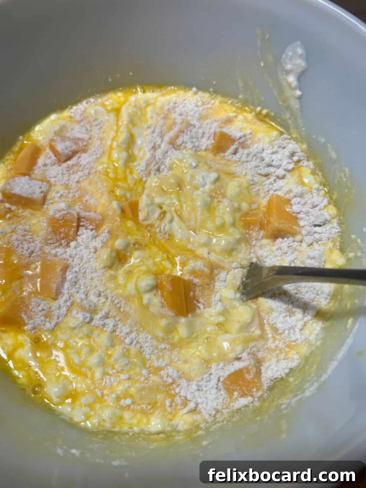Mixing cottage cheese, cubed Cheddar, and flour with beaten eggs in a bowl to create the casserole base.