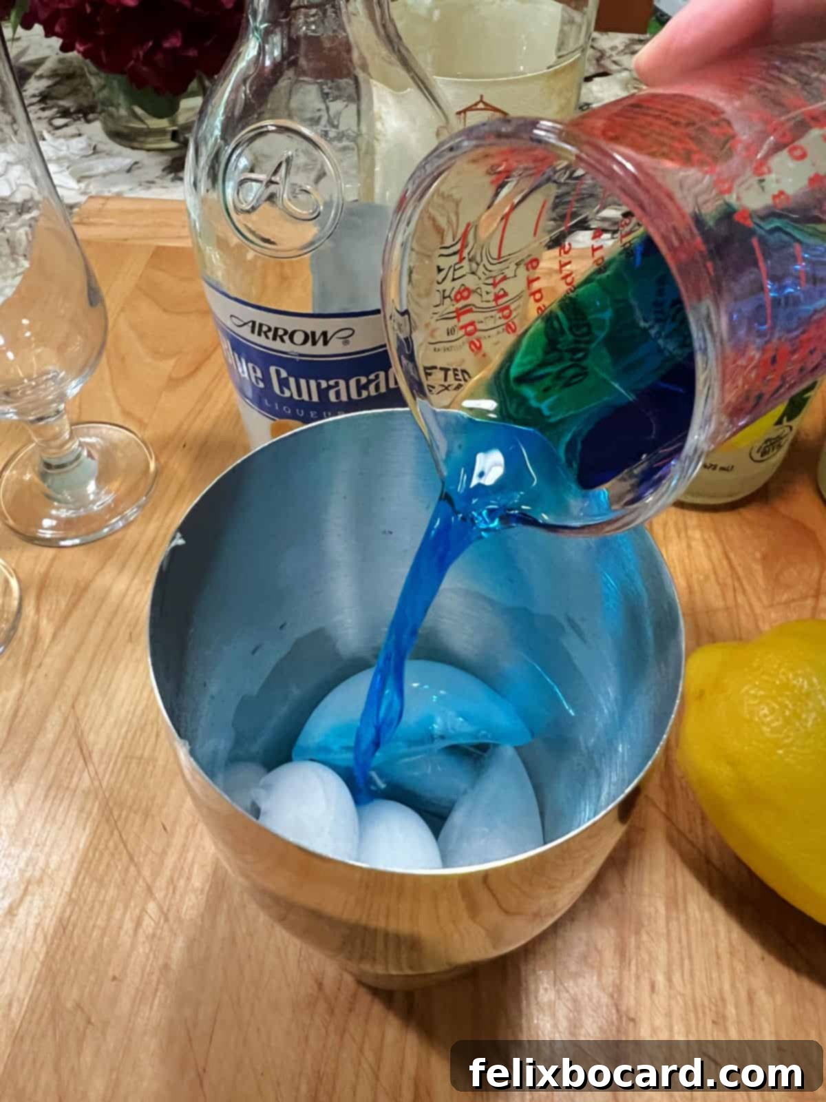 Adding vodka, blue curaçao, and lemonade to a cocktail shaker with ice.