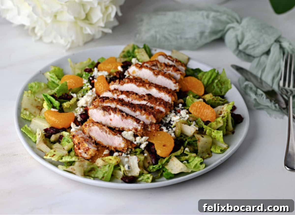 A vibrant Pecan Crusted Chicken Salad featuring golden-brown chicken, fresh greens, mandarin oranges, cranberries, and blue cheese.