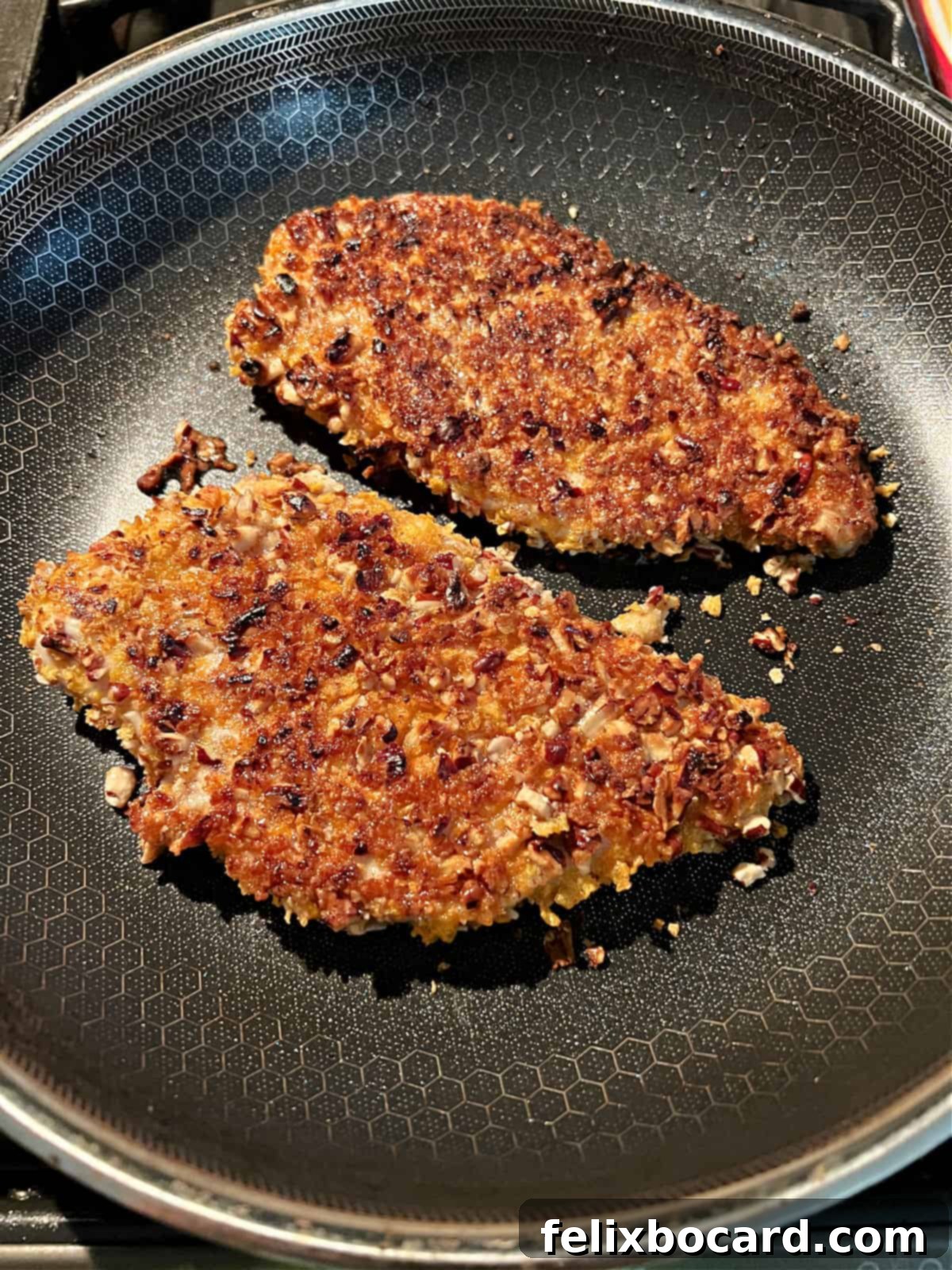 Pecan coated chicken breasts sizzling in a pan, cooking to a golden perfection.