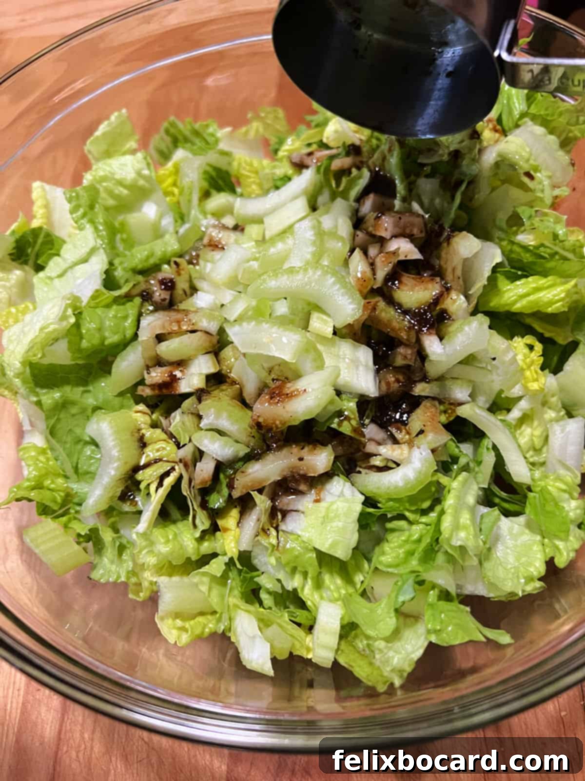 Adding balsamic dressing to a bowl of fresh lettuce and crisp celery, ready to be tossed.