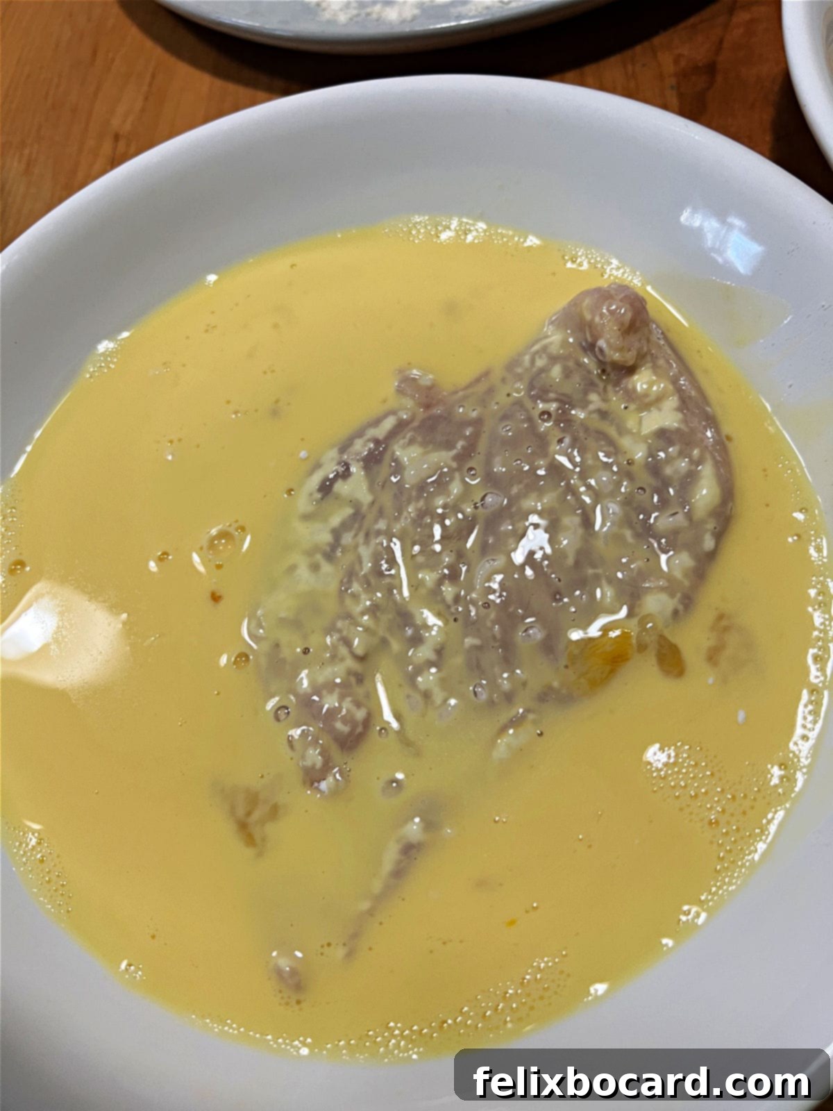 Chicken breast being dipped into the egg and milk mixture.