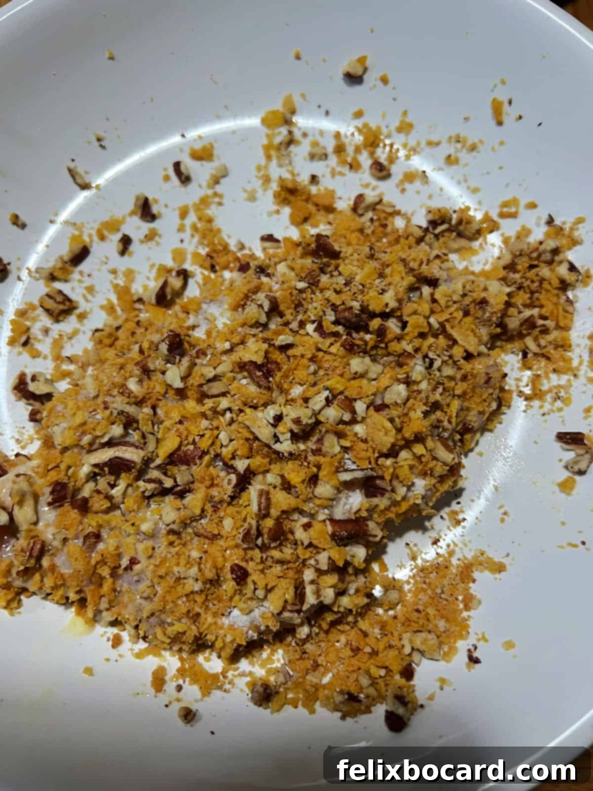Chicken breast being coated with the pecan and cornflake mixture.