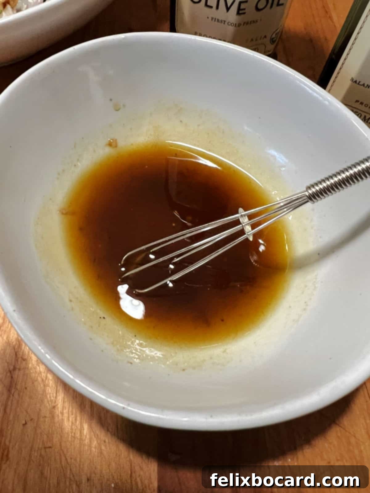 A hand whisking a homemade balsamic vinaigrette in a small glass bowl.
