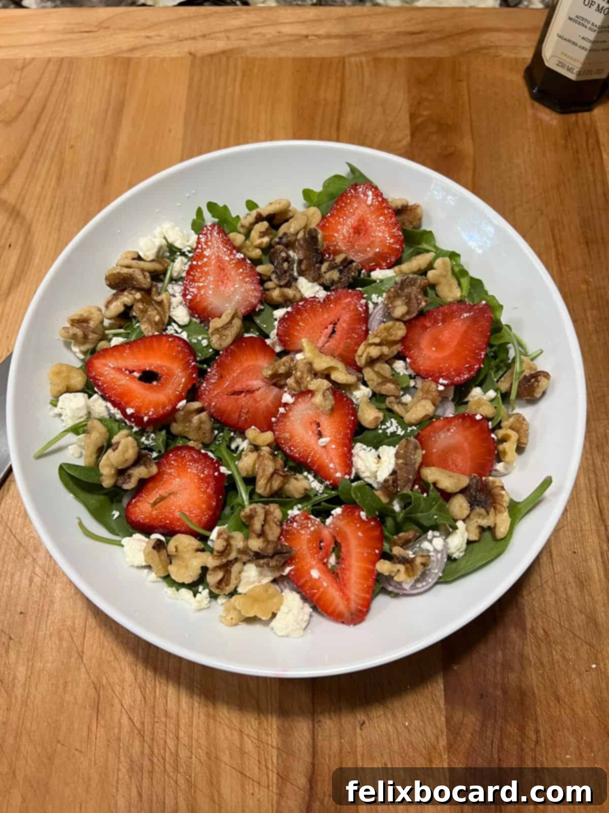 Fully assembled spinach and arugula salad with strawberries, feta, and walnuts, ready for dressing.