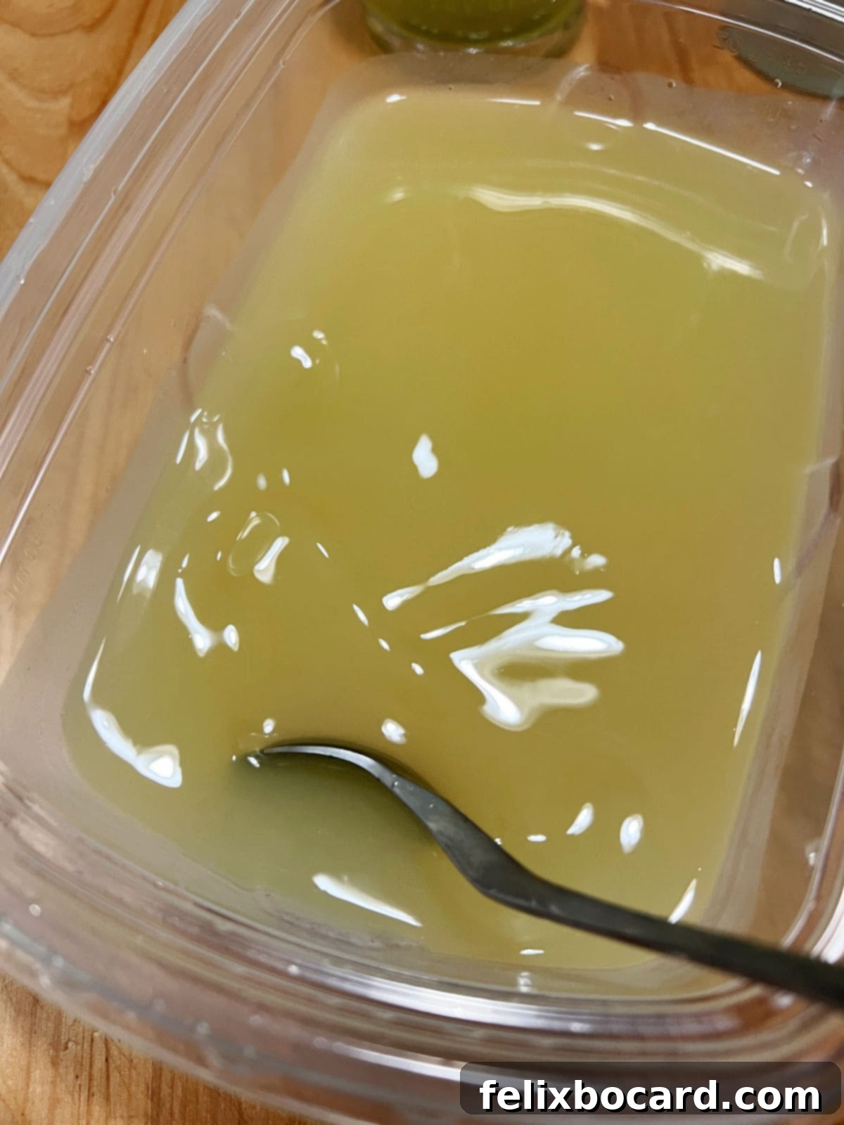 A close-up shot of a hand stirring a vibrant yellow mixture of lemonade concentrate, Limoncello, vodka, and lemonade in a large bowl, preparing for freezing into a delicious slush.