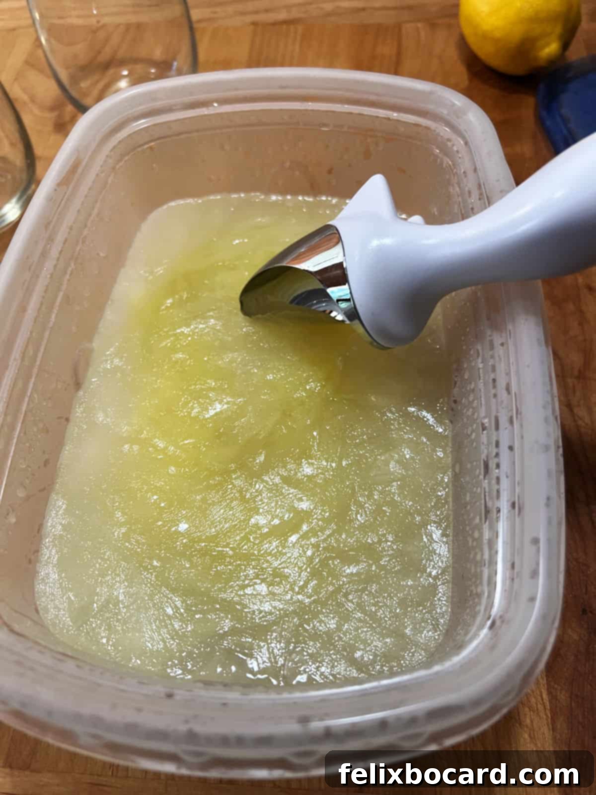 A close-up view of the perfectly frozen, crystalline lemonade slush in a freezer-safe container, showcasing its ideal scoopable texture, ready to be served.