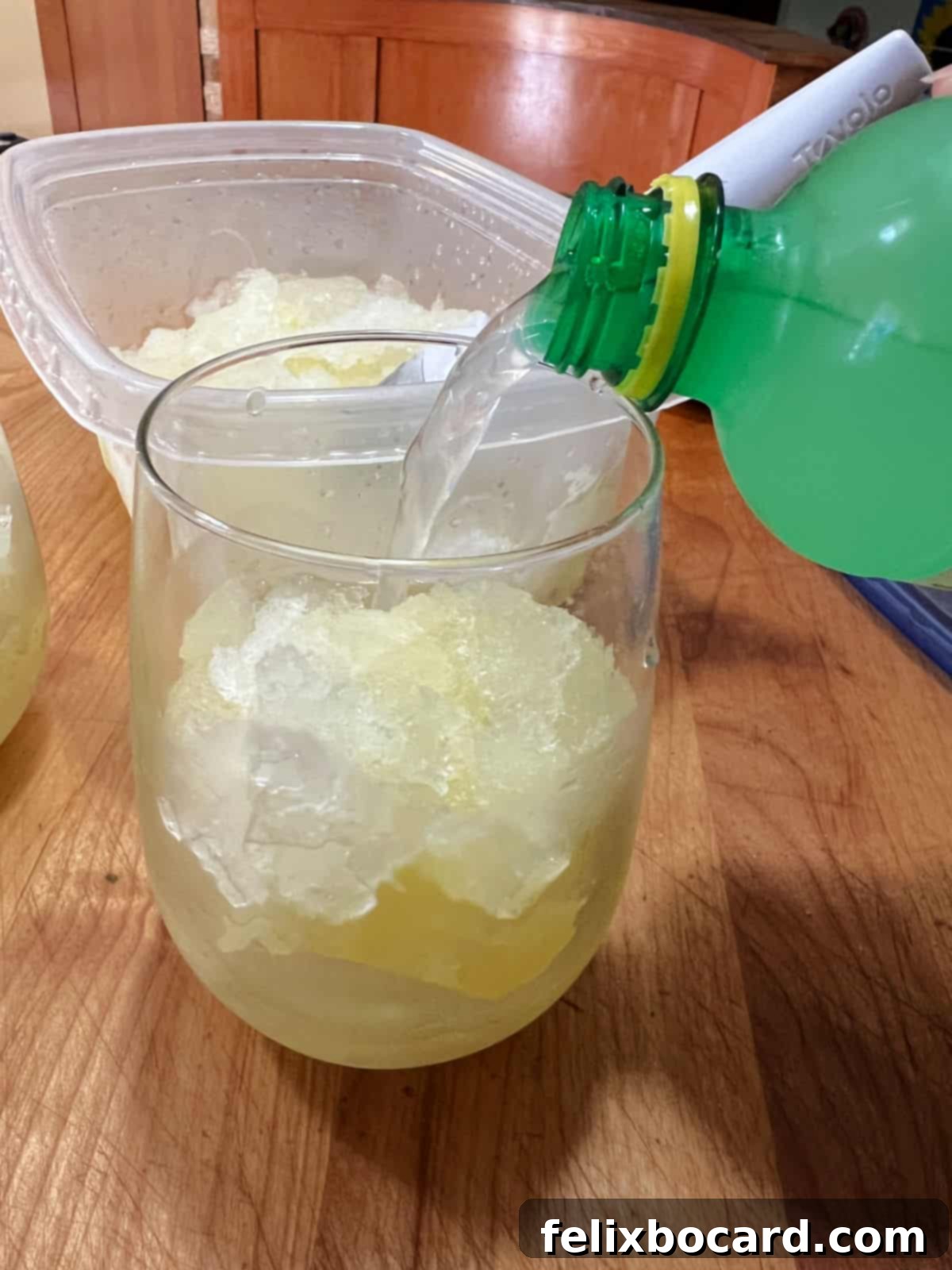 A vibrant frozen lemonade slush being topped with a fizzy lemon-lime soda in a clear glass, creating an inviting, refreshing summer drink.
